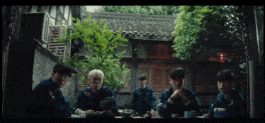 a group of young men sit around a table in front of a brick building
