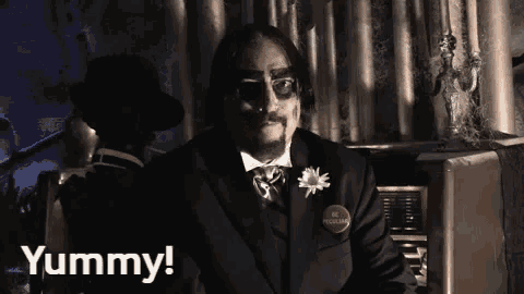 a man in a suit and tie is sitting at an organ and saying yummy