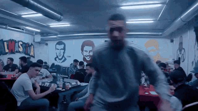 a group of men are sitting at tables in a room with a mural on the wall that says awas tia