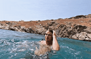 a man is swimming in a body of water near a rocky shoreline