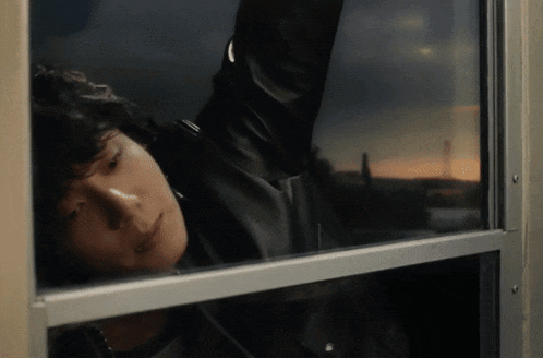 a man in a leather jacket looks out a window at sunset