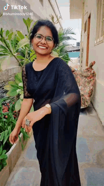 a woman wearing glasses and a black saree is smiling for the camera ..