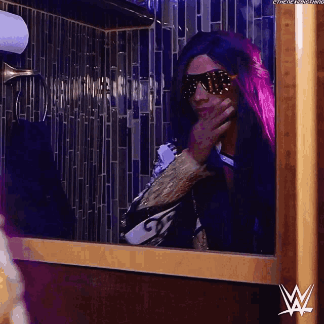 a woman with purple hair is looking at herself in a bathroom mirror