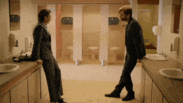 a man and a woman stand in a public restroom