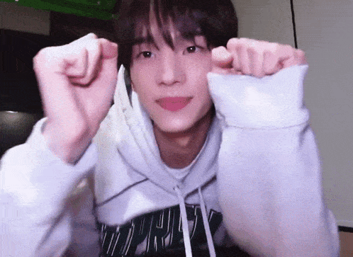 a young man wearing a white hoodie is making a heart shape with his hands .