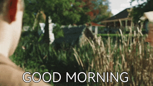 a man is standing in a field with the words `` good morning '' written on the bottom .