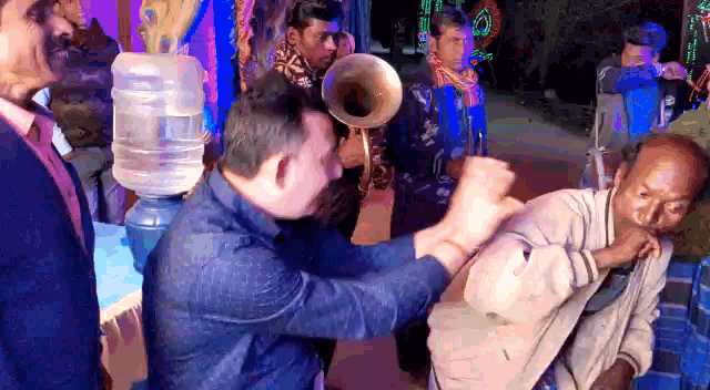 a man playing a trumpet while another man holds a man 's arm in front of a water cooler