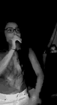 a black and white photo of a woman singing into a microphone in a dark room .