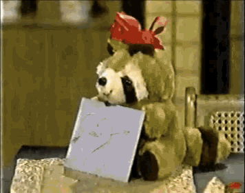 a stuffed animal with a red bow on its head is holding a piece of paper with two hearts drawn on it