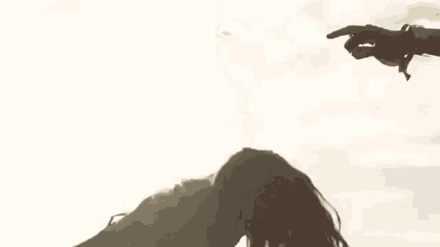 a woman 's hair is blowing in the wind while a man 's hand is pointing at it .