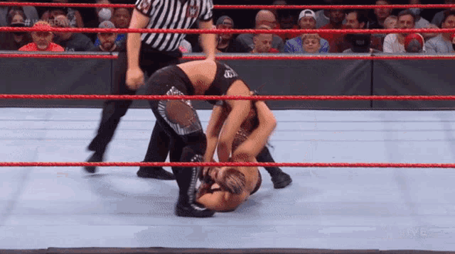 two wrestlers are fighting in a wrestling ring with a referee watching