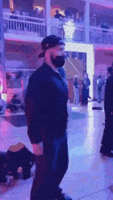 a man wearing a mask and a baseball cap stands in a crowded room