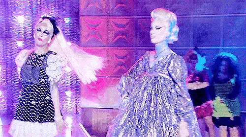 two drag queens are dancing on a stage in front of a crowd of people .