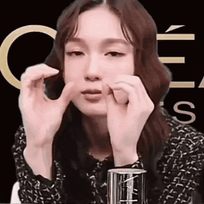 a woman is making a funny face with her hands while sitting at a table .