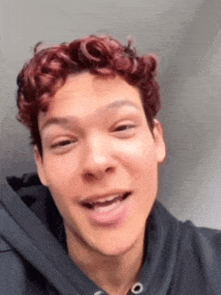 a young man with curly red hair is wearing a black hoodie and smiling .