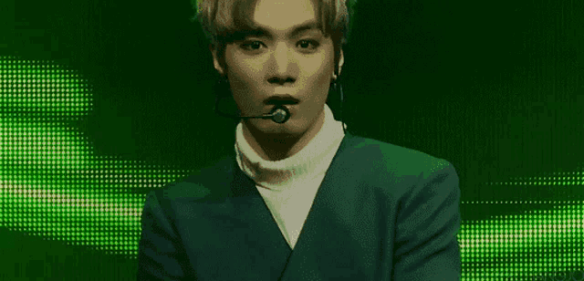 a young man wearing a green jacket and a white turtleneck is standing in front of a green background .