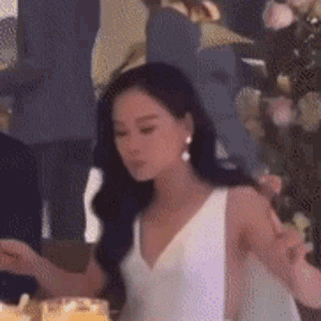 a woman in a white dress is sitting at a table in front of a cake .
