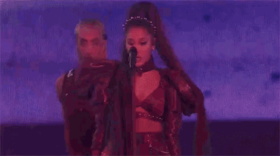 a woman is singing into a microphone while a man stands behind her