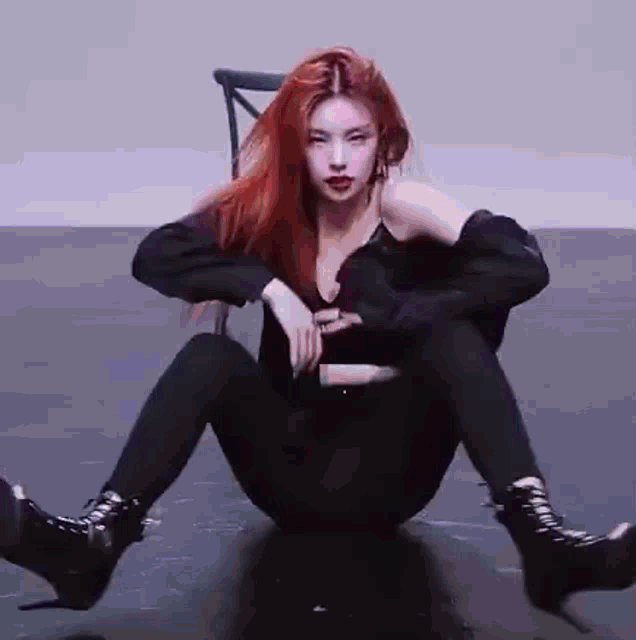 a woman with red hair is sitting on the floor with her legs crossed and a chair in the background .