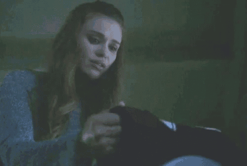 a woman is sitting on a toilet in a dark room holding a shirt .