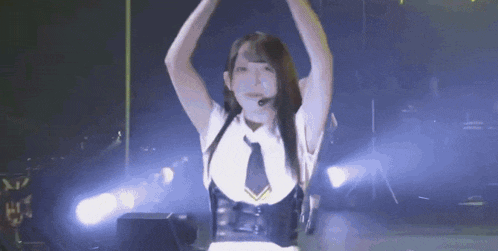 a woman in a white shirt and black tie is dancing on a stage with her arms in the air