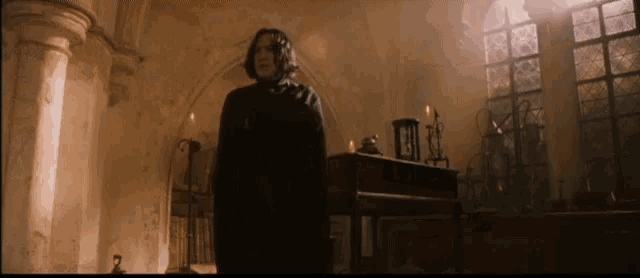 a man in a black cape stands in a dark room with candles
