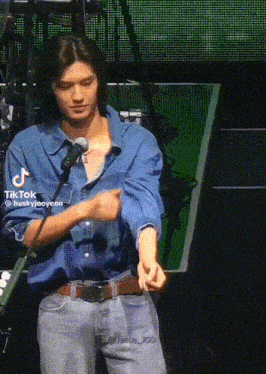 a man in a denim shirt is standing in front of a microphone ..