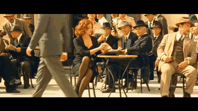 a woman sitting at a table with a man walking by