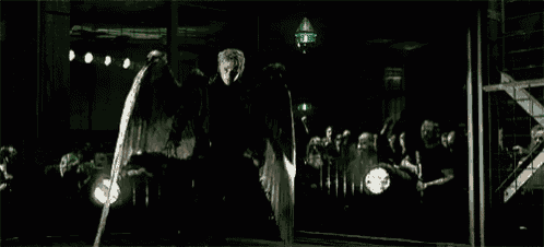 a man with wings is standing in front of a crowd of people in a dark room .