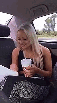 a woman is sitting in the back seat of a car holding a cup of soda