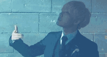 a man in a suit and tie is giving a thumbs up in front of a brick wall .