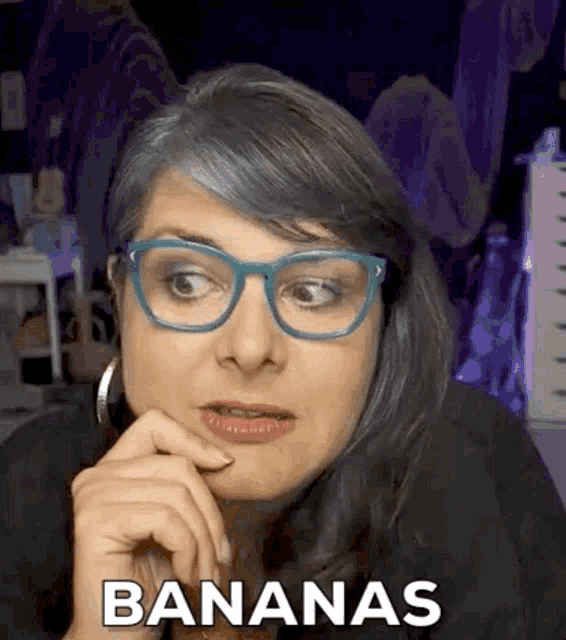 a woman wearing glasses and earrings is making a funny face and saying bananas .