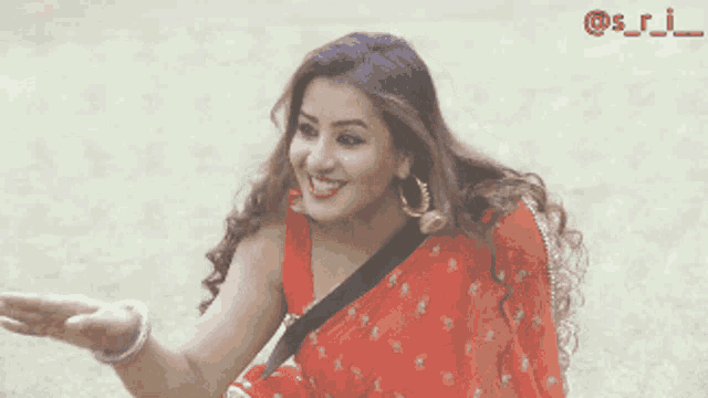 a woman in a red saree is smiling and reaching out towards the camera