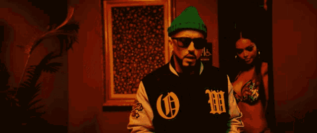 a man wearing sunglasses and a varsity jacket with the letter h on the sleeves