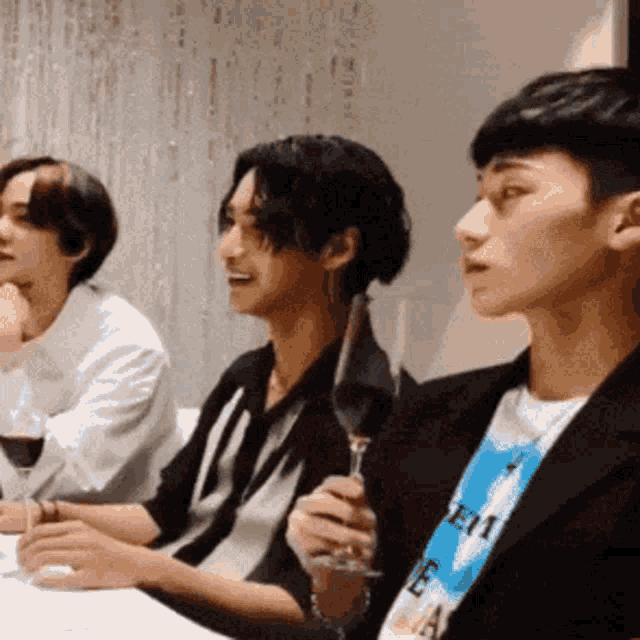 a group of young men are sitting at a table drinking wine and talking