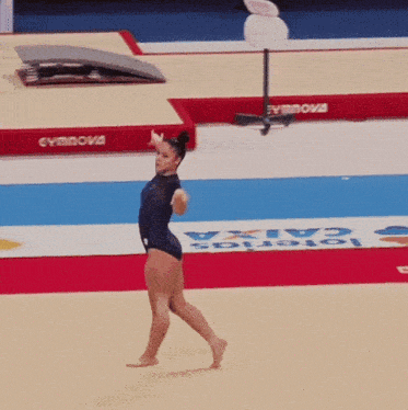 a female gymnast performs on a gym floor with a caixa sign in the background