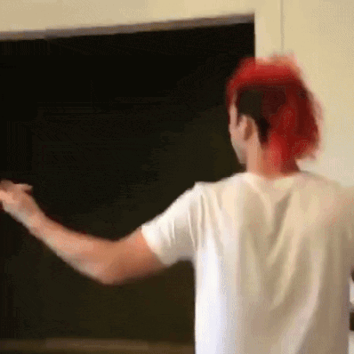 a man with red hair is standing in front of a blackboard with his arms outstretched .