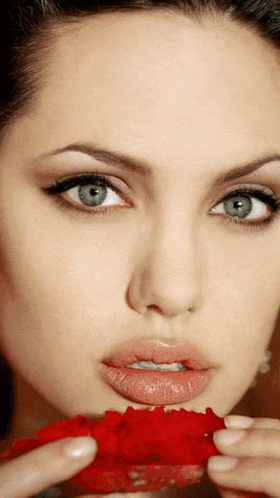a close up of a woman 's face with green eyes holding a red rose