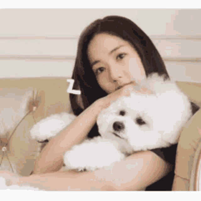 a woman is sitting on a couch with a small white dog .