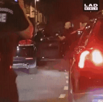 a group of police officers are standing in front of a red car on a street .