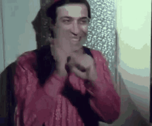 a man in a red shirt and hat is making a funny face while clapping his hands .