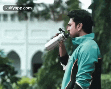 a man in a blue jacket is drinking water from a water bottle .