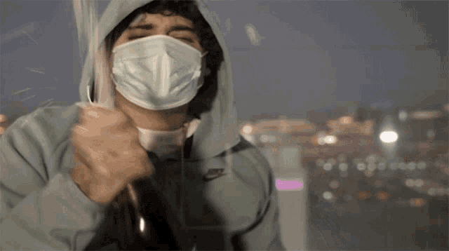 a man wearing a mask and a nike hoodie is holding an umbrella