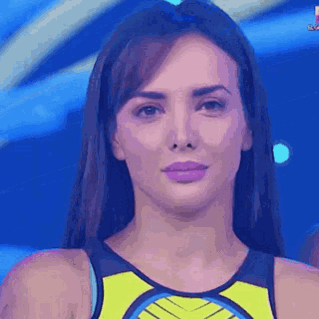 a close up of a woman 's face with a blue background and a yellow tank top .