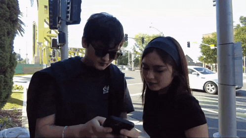 a man and a woman are looking at a cell phone while standing on a street