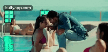 a man is kissing a woman in a bikini while sitting next to a pool .