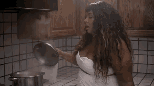 a woman in a white towel is standing in a kitchen holding a pot .