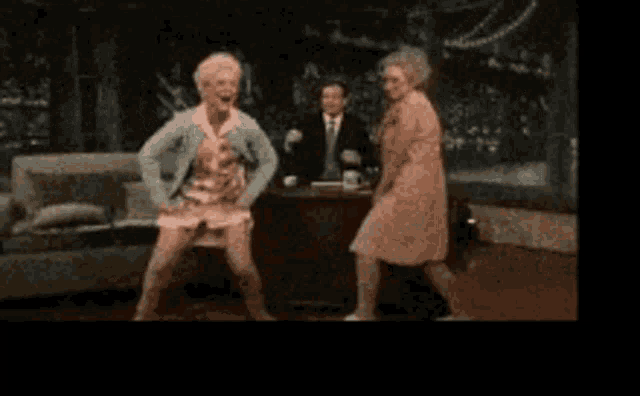 two older women are dancing in front of a man in a suit and tie