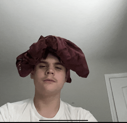 a young man wearing a white shirt and a burgundy shirt on his head
