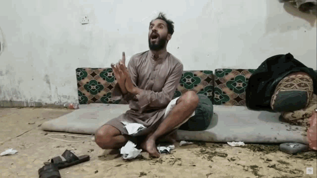 a man with a beard is sitting on the floor with his hands in his pockets